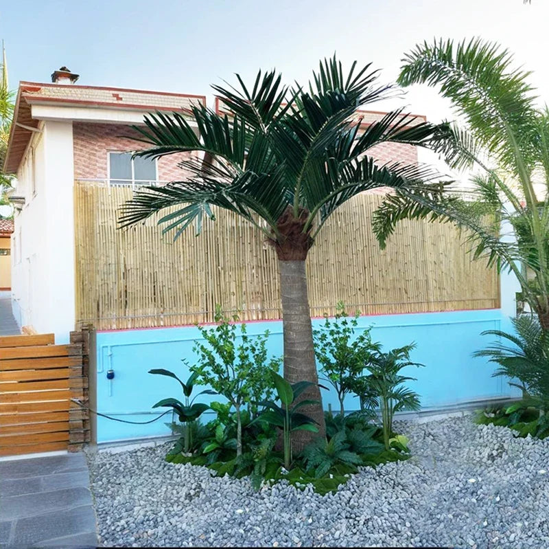 The artificial fan palm planted outdoors beside a paved entrance walkway