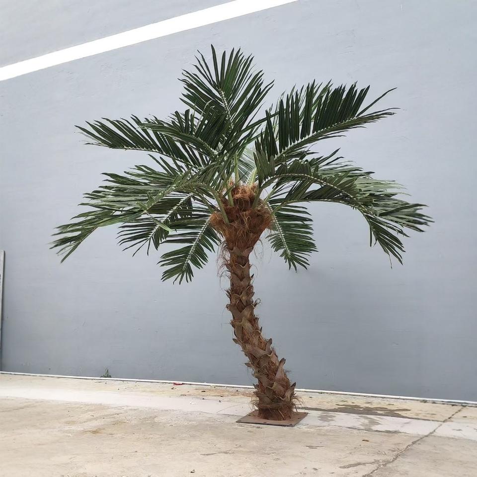 Large artificial palm with a curved trunk effect, fronds arching over from the crown
