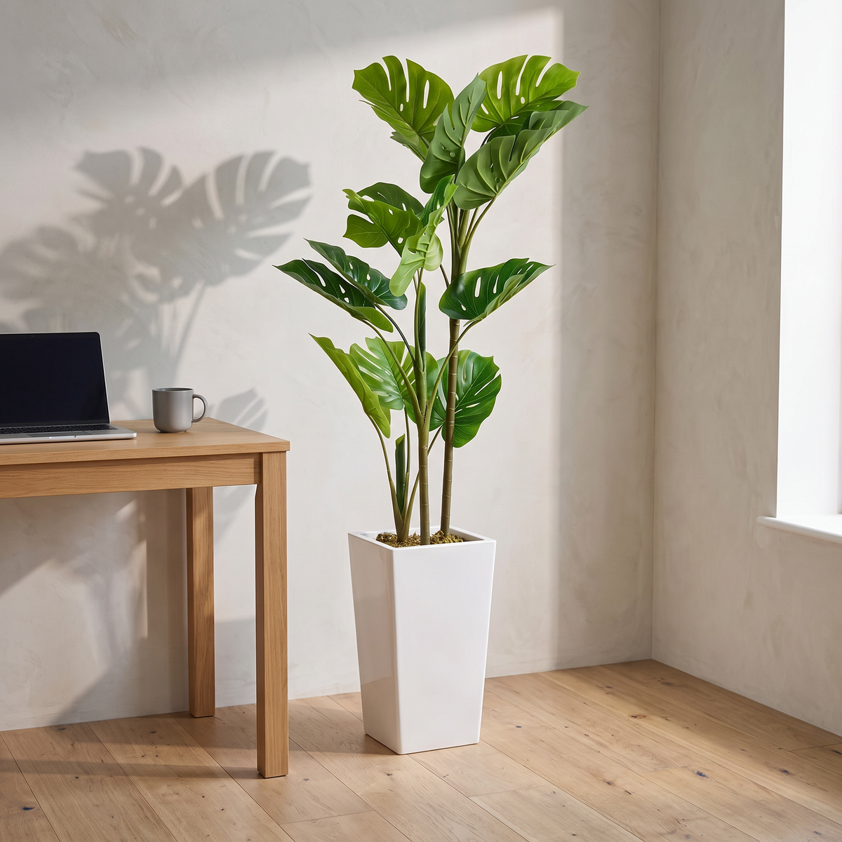 Artificial monstera plant with split leaves in a cement-filled white planter